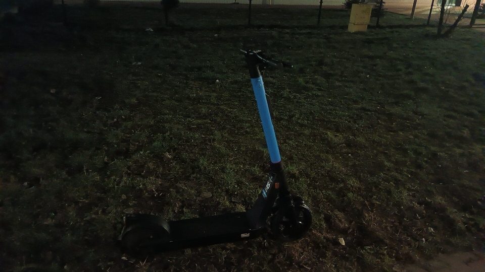 Trottinette électrique bleue posée sur une zone herbeuse en soirée