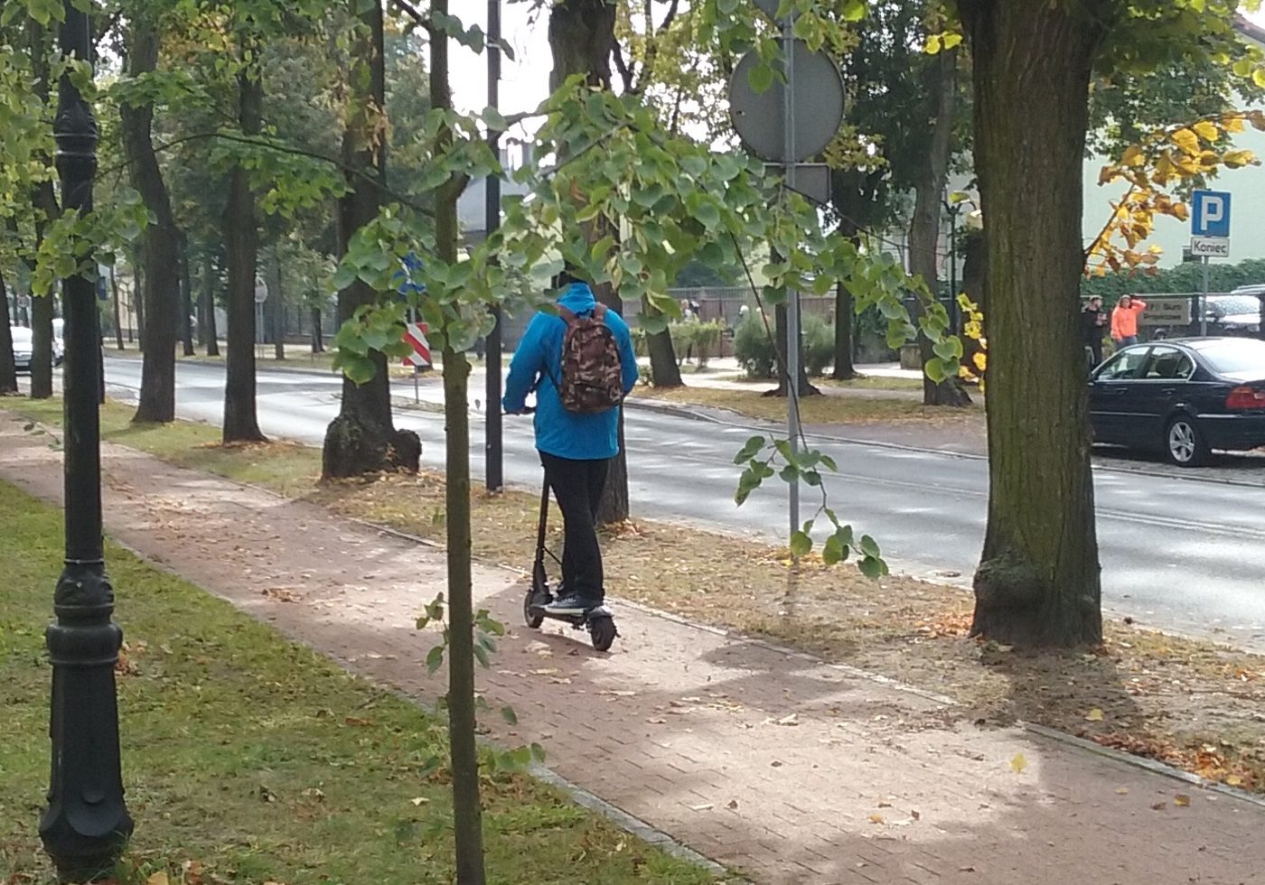 Conducteur en trottinette électrique sur une allée urbaine arborée