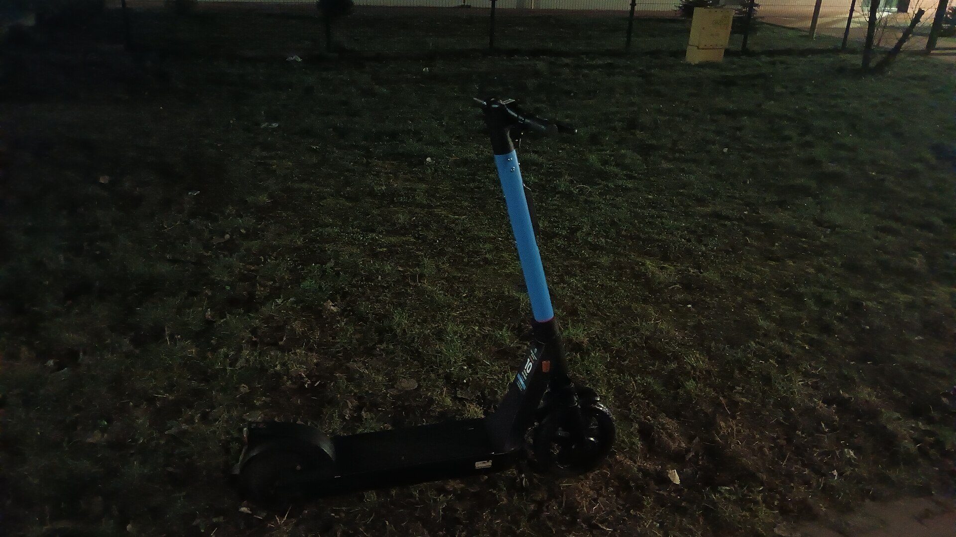 Trottinette électrique bleue posée sur une pelouse en ville